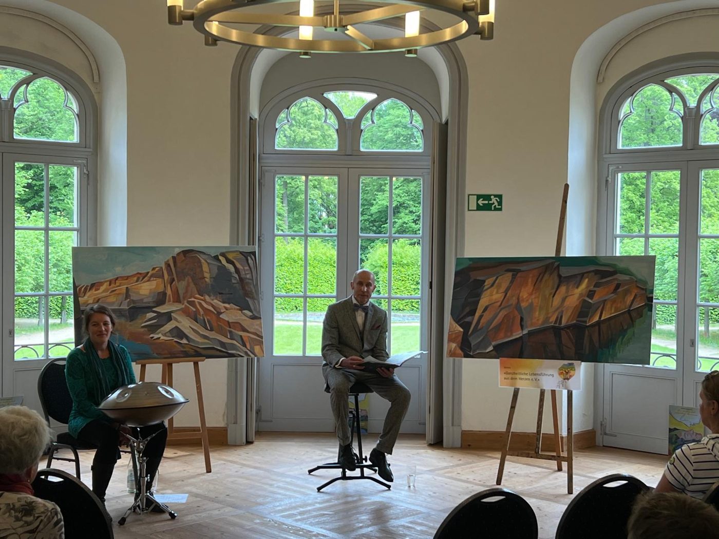 Robert Brodhun liest im Schloss Königshain, daneben Anne Kern mit der Handpan und ihre Bilder auf Staffeleien